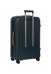 Valigia rigida di colore blu navy, caratterizzata da scanalature verticali, manico estraibile, dettagli marroni e quattro ruote girevoli per una facile mobilità.