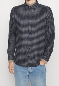 Camicia a quadri blu navy e grigia realizzata in tessuto morbido, con chiusura a bottoni, colletto, taschino sul petto e dettagli con maniche arrotolate.