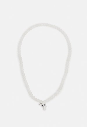 Collier de perles blanches avec un pendentif crâne en argent portant des lunettes de soleil et une petite étiquette portant l'inscription "KARL."