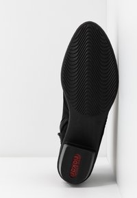 Semelle de chaussure noire avec un motif de semelle ondulé, taille 37, et logo "rieker" rouge sur le talon, positionnée contre un fond blanc en coin.