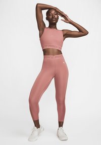 Riblasti sportski crop top i visokotalasne tajice od mekane ružičaste tkanine s teksturiranim pojasom koji sadrži "NIKE PRO" logo i kontrastne šavove.