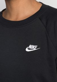 Svart sweatshirt med ribbat halsband och en vit broderad Nike-logotyp på övre vänstra bröstet. Mjukt bomullsmaterial med en avslappnad passform.