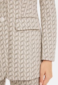 Light gray suit jacket featuring a geometric pattern, textured fabric, notched lapel, and a front pocket with rounded flap.