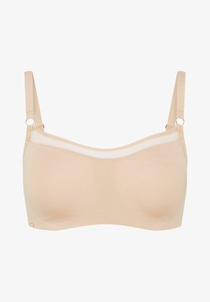 Beżowy bezprzewodowy stanik z miękkiego materiału, przezroczym górnym brzegiem i regulowanymi ramiączkami z okrągłymi elementami metalowymi dla wsparcia i elastyczności.