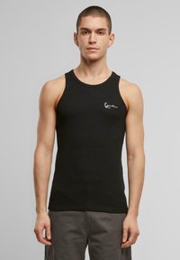 Schwarzes, geripptes Tanktop mit rundem Ausschnitt, das ein kleines weißes Logo auf der linken Brust trägt. Hergestellt aus weicher, leichter Baumwolle.
