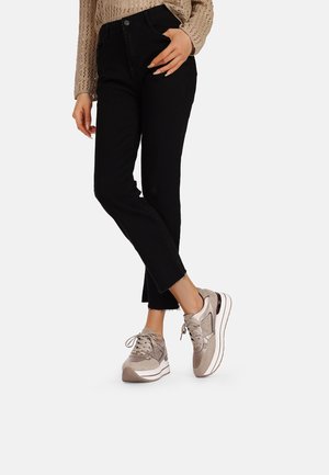 Jeans neri a vita alta con orlo sfilacciato abbinati a sneakers grigio chiaro con dettagli in rete e lisci. Top in maglia casual visibile.