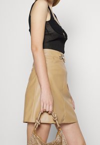 Schwarzes geripptes Oberteil mit tiefem Ausschnitt, kombiniert mit einem beigen Leder-Minirock mit einer dekorativen Gürtelschnalle und einer goldenen Handtasche.