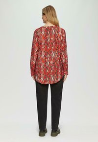 Rode slangenprint blouse met lange mouwen en een afgeronde zoom, gemaakt van soepel materiaal, gecombineerd met zwarte broek en stevige zwarte laarzen.