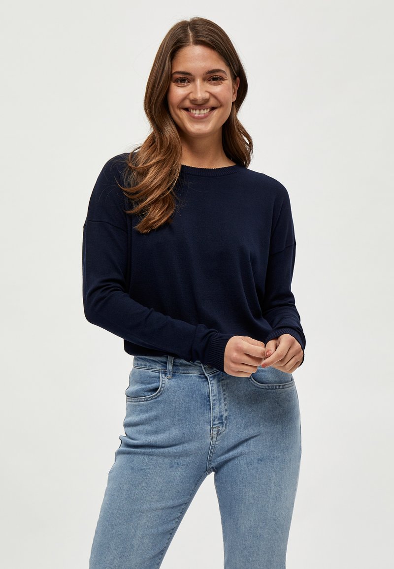 Pull en maille marine à manches longues et col rond, associé à un jean lumière bleu ajusté. Texture douce et coupe décontractée.