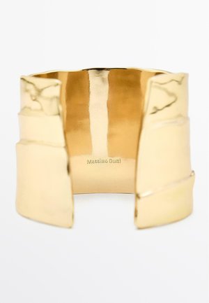 Bracciale in cuff d'oro con finitura lucida. Presenta un design ampio, forme geometriche e una sottile incisione che recita "Massimo Dutti".