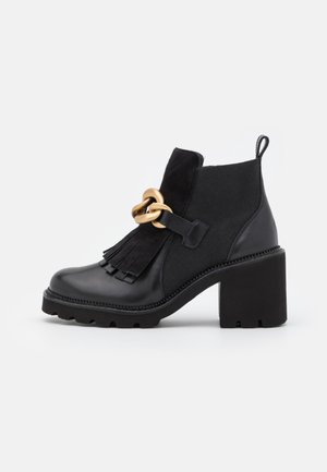 Bottes noires à la cheville avec un talon épais, présentant un bout en cuir, des accents en daim, un détail frangé et une décoration en chaîne dorée sur le côté.