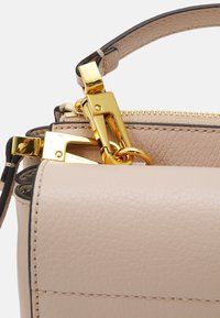 Lys beige lærveske med en strukturert form, som har gullfarget tilbehør, glidelås og en buet topphåndtak.