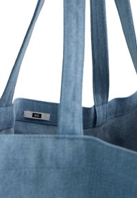 Denim auduma soma ar divām izturīgām siksnām, gaiši zila krāsa un iekšējais etikets. Mīksta tekstūra un vienkāršs dizains, piemērota ikdienas lietošanai.