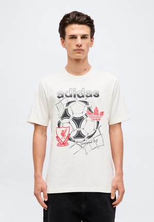 Νέος άνδρας που φοράει λευκό t-shirt Adidas με ασπρόμαυρη ποδοσφαιρική μπάλα, το έμβλημα της Liverpool FC και κόκκινο λογότυπο Adidas.