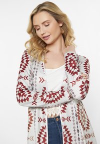 Geometrisch gemusterter Cardigan in Hellgrau mit roten und braunen Akzenten. Offene Vorderseite mit langen Ärmeln und lockerer Passform.