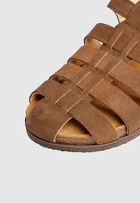 Braune Wildledersandale mit mehreren überkreuzten Riemen, offenem Zehendesign, gepolstertem Fußbett und strukturiertem Gummisohle.