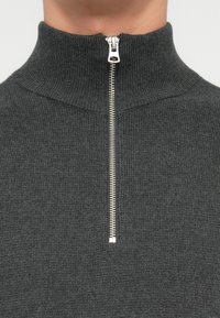 Maglione grigio a collo alto lavorato a maglia con chiusura a zip, caratterizzato da una texture a coste e una cerniera liscia di colore argento.