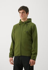 Veste à capuche zippée verte avec un design ajusté, capuche et poche avant. Fabriquée dans un tissu texturé avec des accents noirs et un logo sur la poitrine.
