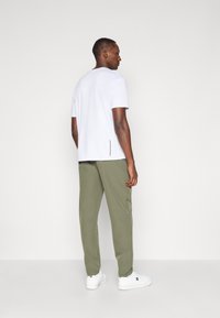 White short-sleeve t-shirt with a relaxed fit, paired with light olive green pants, and white sneakers. Features minimal design and smooth texture.
