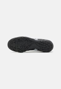 Suola di scarpa sportiva nera con vari modelli testurizzati e tacchetti per una migliore aderenza. Il materiale sembra gommoso con una superficie liscia.