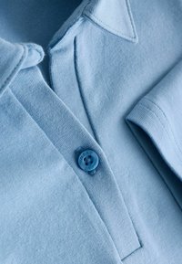 Svetlomodré tričko polo z jemnej bavlny, s légou so svetlomodrým gombíkom označeným "NEXT" a rebrovaným golierom a manžetami.