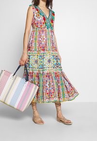 Maxi dress floreale colorato con scollatura a V e spalline arricciate, abbinato a una borsa a tracolla a righe nei toni pastello. Sandali beige.
