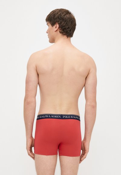 Raudonos medvilninės bokserės su tamsiai mėlynu liemeniu ir baltu užrašu „POLO RALPH LAUREN“. Modelis rodomas iš nugaros, matomas apvilkimo stilius ir dizainas.