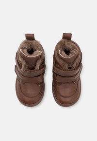 Bottes en cuir marron avec deux bandes Velcro, doublure intérieure douce, bout arrondi et coutures renforcées le long de la semelle.