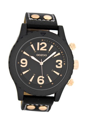 Montre noire avec un cadran rond, des chiffres dorés et trois boutons sur le côté. Elle possède un bracelet en cuir noir texturé avec des accents dorés.