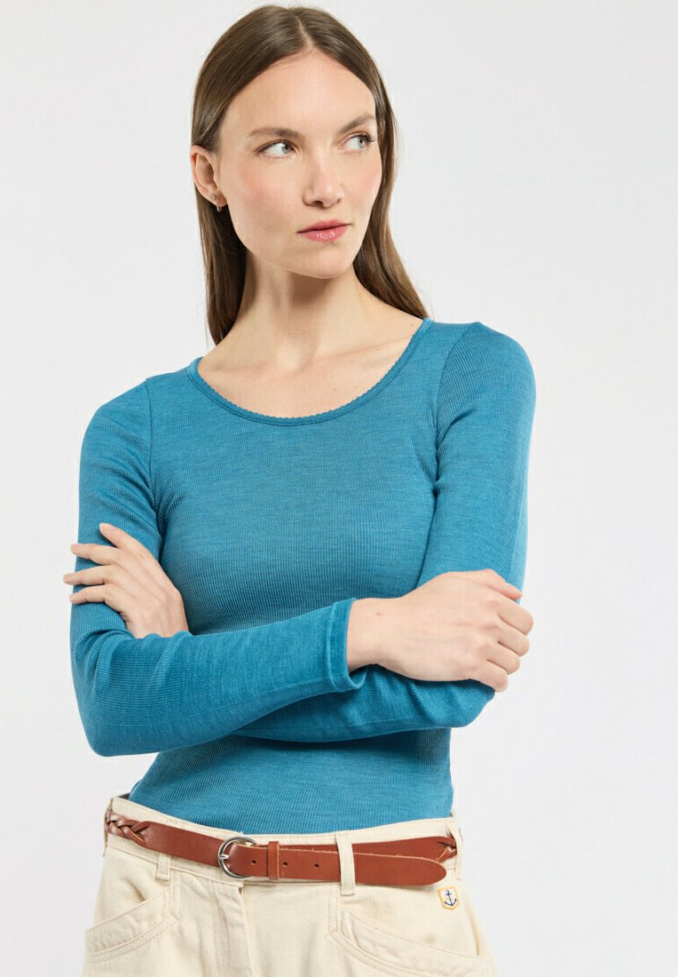 Haut long à manches ribbées de couleur sarcelle avec un col rond et une coupe ajustée. Assorti à une ceinture beige clair et un bas beige, avec un détail en forme d'ancre.