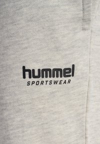 Hellgrauer Sweatstoff mit einem auffälligen schwarzen "hummel"-Logo und dem Text "SPORTSWEAR". Strukturierter, weicher Stoff mit einem lässigen Design.