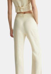 Pantaloni in lino color crema con taglio dritto, dotati di una chiusura con zipper sul retro e una finitura liscia e strutturata.