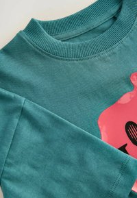 Türkises Baumwoll-Sweatshirt mit einem runden, gerippten Ausschnitt, langen Ärmeln und einem glänzenden pinken Grafikdesign mit schwarzen Akzenten.