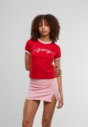 Chemise rouge à manches courtes avec des accents roses et le texte "juicy" en cursive blanche, associée à une mini-jupe rose avec une fente sur le côté et un détail froncé.