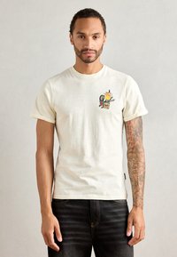 Cremefarvet bomulds t-shirt med et farverigt grafiktryk med flammer og et design på venstre bryst. Korte ærmer, simpel snit.