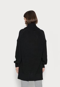 Černý pletený rolák s volným střihem, ribbovanou texturou a oversized rukávy, s rovnými lemy a jemnými švy.