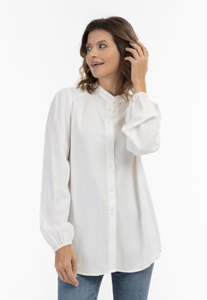 Witte blouse met lange mouwen en hoge nek, met knopen aan de voorkant en geplooide manchetten. Zachte stof met een gladde textuur, gecombineerd met jeans.