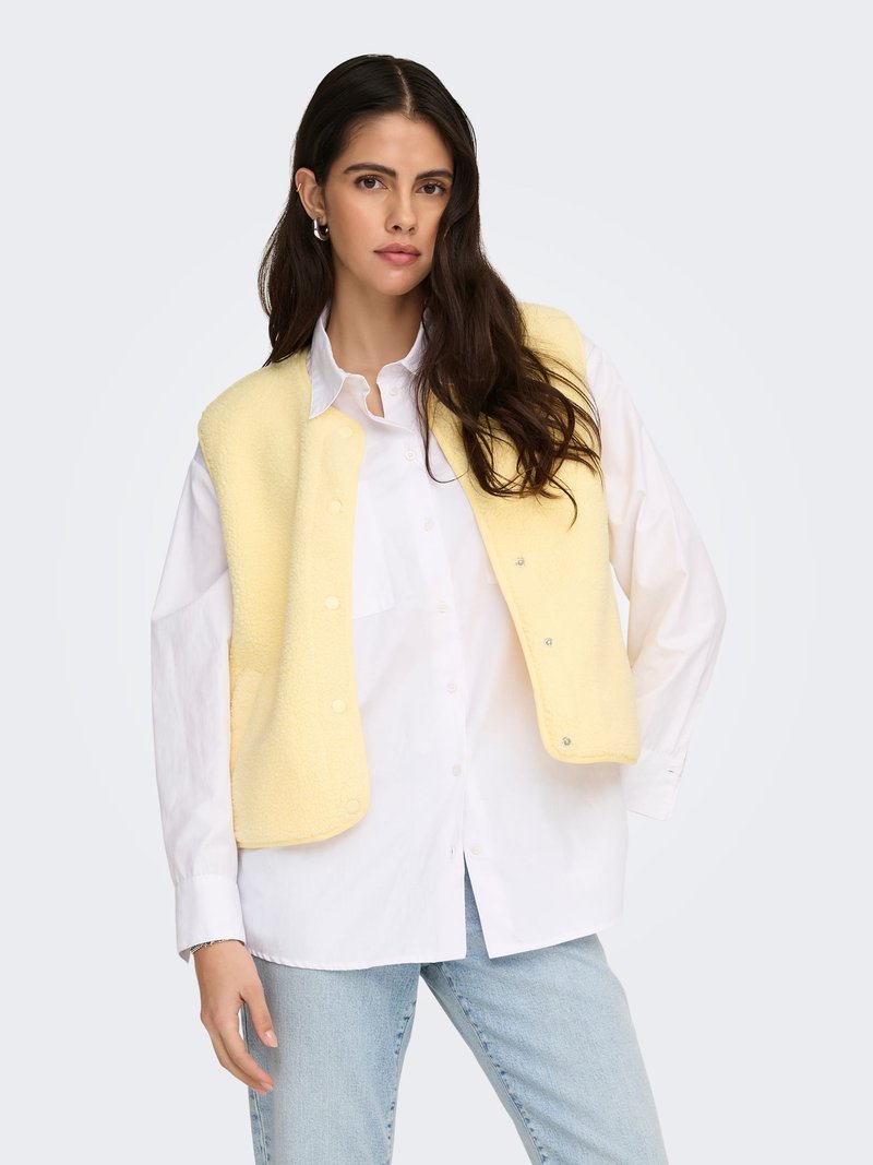 Geelt fleecesvest met drukknoopsluiting over een wit overhemd met knopen, gecombineerd met lichtblauwe spijkerbroek. Glad oppervlak, comfortabele pasvorm.