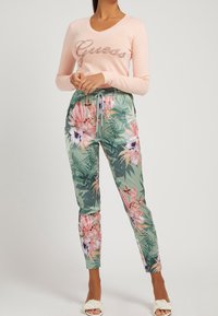 Top de manga larga color rosa claro con la palabra "Guess" en lentejuelas, combinado con pantalones verdes con estampado floral que incluyen flores rosas y moradas, y cintura con cordón.