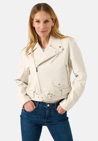 Weiße Leder-Motorradjacke mit Gürtel in der Taille, Reißverschlusstaschen und einem asymmetrischen Schnitt. Getragen mit blauen Jeans.
