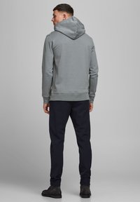 Sudadera gris clara con una gran capucha y dobladillo acanalado, combinada con pantalones oscuros a rayas y botas negras hasta el tobillo. Textura de tela suave.