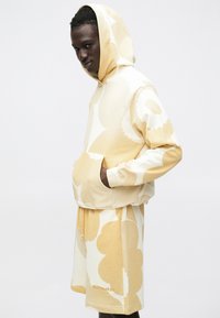 Conjunto de sudadera con capucha y pantalones cortos en algodón suave, con un gran patrón floral en tonos crema y amarillo claro, con bolsillo tipo canguro.