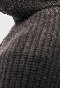 Maglione lavorato a maglia grigio scuro con una texture a coste, colletto alto e tessuto morbido che ne esalta l'aspetto accogliente.