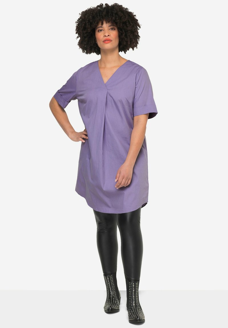 Paars korte jurk met v-hals en voorplissé, gecombineerd met zwarte leggings en gestudde enkelboots. Gladde, lichte stof.