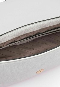Interior de un bolso de cuero blanco con una textura suave. El forro marrón presenta rayas diagonales. Detalle de hardware dorado visible en la parte inferior.