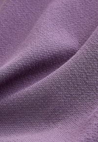 Tissu violet doux et texturé avec un motif subtil en relief de type gaufré et des plis délicats créant des ombres et de la profondeur.