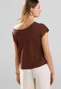 Top marron oversized à manches courtes avec un large col. Texture lisse, coupe décontractée ; associé à un pantalon beige clair.