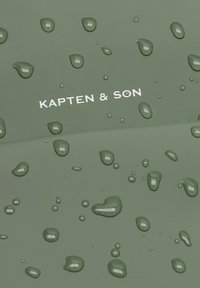 Wasserabweisender grüner Stoff mit Tropfen, versehen mit dem Text "KAPTEN & SON" in Weiß. Glatte Textur mit matter Oberfläche.
