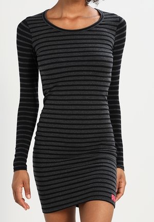 Vestido ajustado con rayas horizontales negras y gris oscuro, mangas largas y cuello redondo, llevado por una persona de pie.