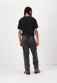 Black t-shirt with short sleeves, paired with gray distressed denim jeans, featuring an elastic waistband and two back pockets. Black and white sneakers.